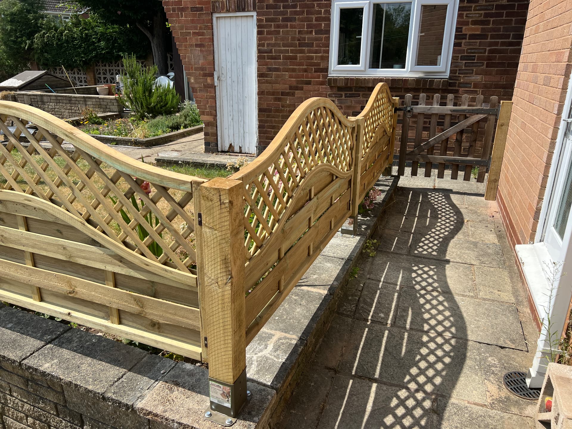 Close view of completed timber fence panels and posts fixed to the wall on metal post supports