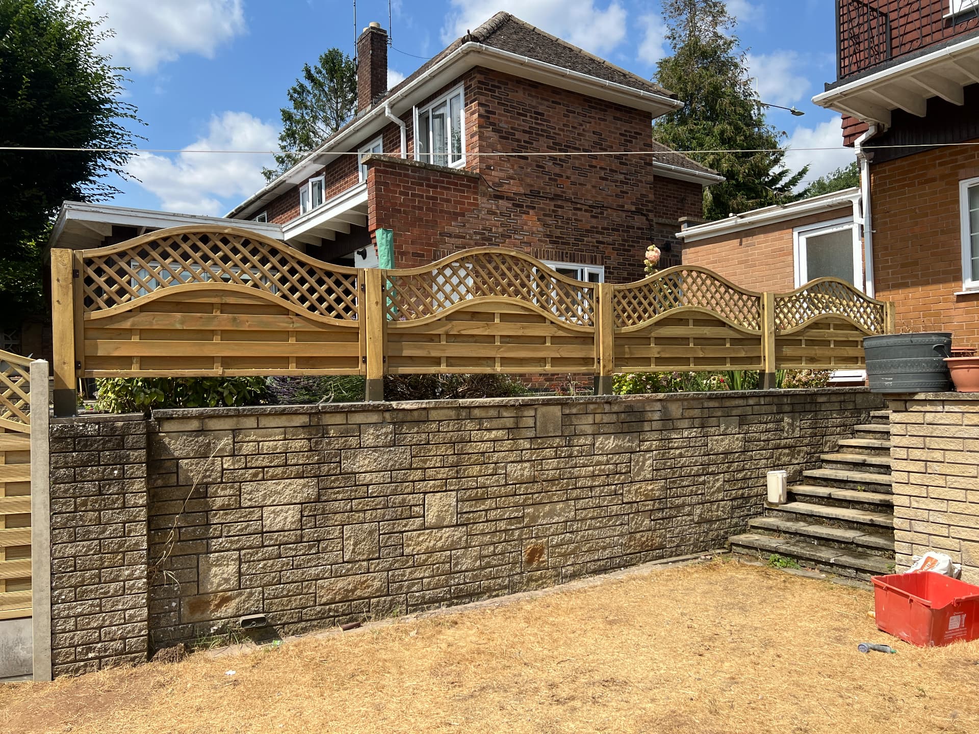 Completed run of wave-top lattice timber fence panels fitted along a raised garden wall